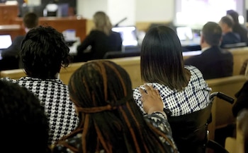Vista posterior de varias personas sentadas en un recinto judicial y una mano apoyada sobre el hombro de una mujer