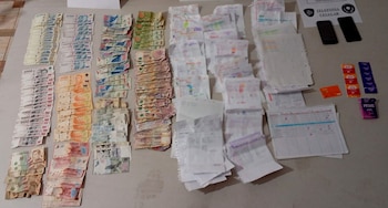 Una vista aérea de dinero en efectivo apilado, papeles escritos, dos teléfonos celulares, una tarjeta de crédito y condones sobre una mesa clara