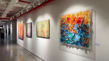 Pasillo de galería de arte con paredes blancas y techo de tubos rojos. Cuatro obras exhibidas, una escultura tridimensional colorida y tres pinturas rectangulares