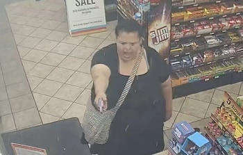 Vista superior de una mujer con camiseta negra y bolso a rayas apuntando un objeto pequeño y violeta hacia el frente dentro de una tienda