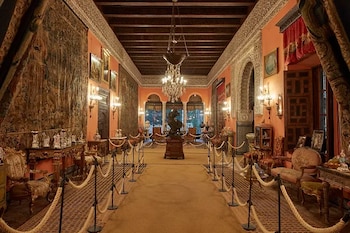 Interior de un gran salón en el Palacio de las Dueñas, con tapices en las paredes, muebles ornamentados, un candelabro y una alfombra central que guía a una estatua