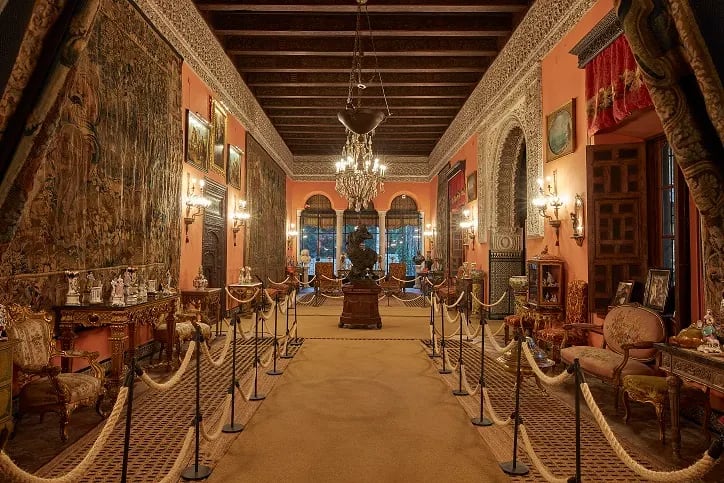 El impresionante salón principal del Palacio de las Dueñas en Sevilla, adornado con tapices, mobiliario antiguo y elementos decorativos.