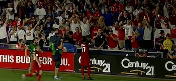 Jozy Altidore, de espaldas, con una camiseta roja número 17, en un campo de fútbol. Levanta los brazos frente a una multitud de aficionados y vallas publicitarias