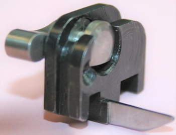 Primer plano de un pequeño dispositivo negro y metálico con componentes cilíndricos y una palanca lateral, sobre un fondo claro