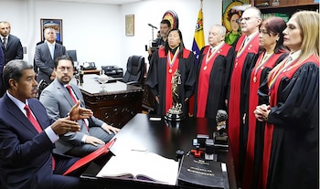 Nicolás Maduro sentado habla frente a un grupo de magistrados con togas judiciales en una oficina con la bandera de Venezuela