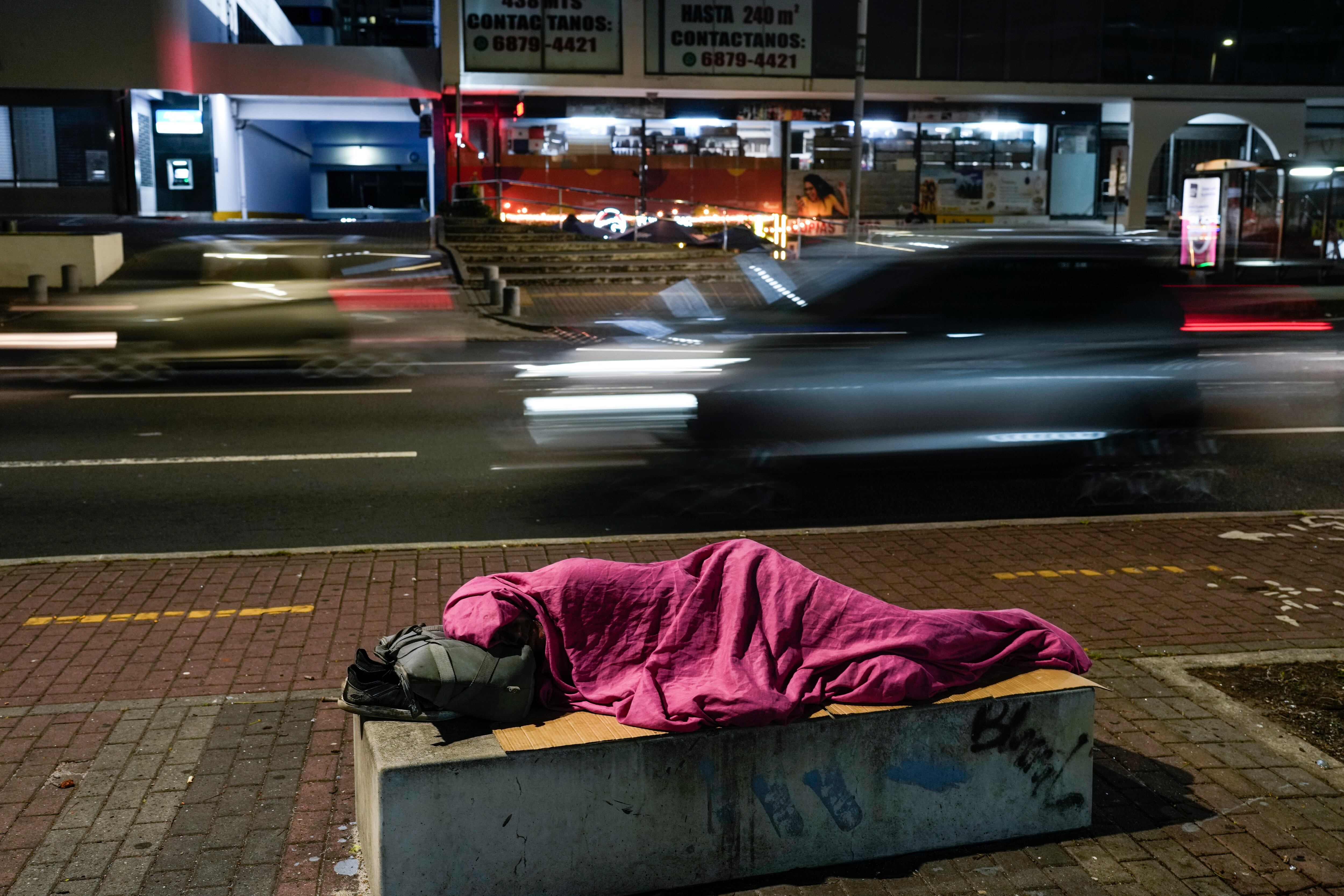 Una persona duerme en un banco de concreto junto a una calle en la Ciudad de Panamá. (Foto AP/Matías Delacroix)