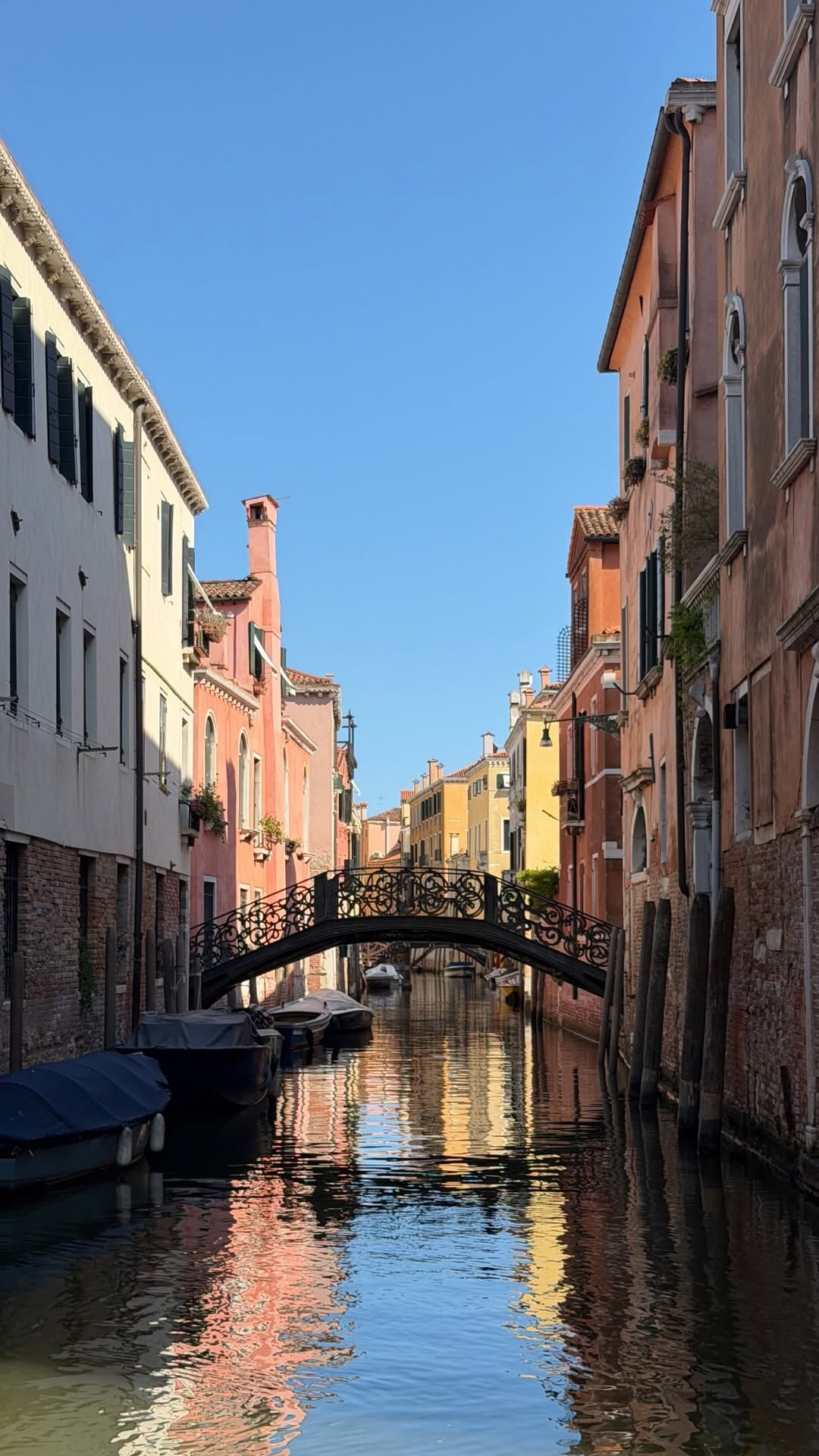 Un canal de Venecia con edificios históricos de colores variados, cruzado por un puente de hierro forjado
