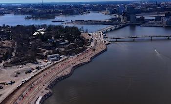 Fotografía aérea de una zona costera urbana con vías de tranvía, un paseo con personas, múltiples puentes sobre el agua y edificios de la ciudad al fondo
