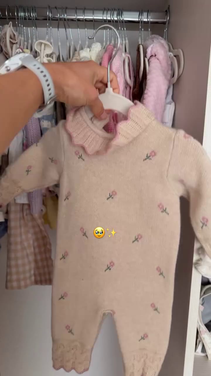 Julieta Puente exhibe un mameluco beige de bebé con bordados florales en rosa, parte de los preparativos para la llegada de su primera hija