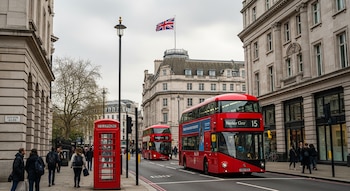 Calle de Londres con autobús rojo de dos pisos, cabina telefónica roja, peatones y edificios históricos. La bandera del Reino Unido ondea sobre un edificio.