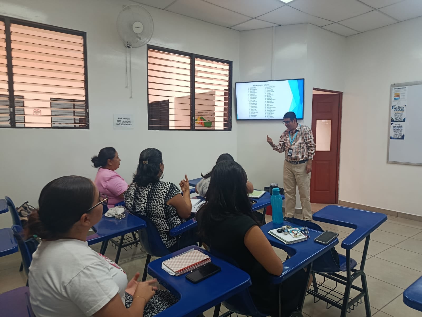 Una ponente expone ante un grupo de asistentes que levantan las manos durante un seminario de capacitación en un aula.