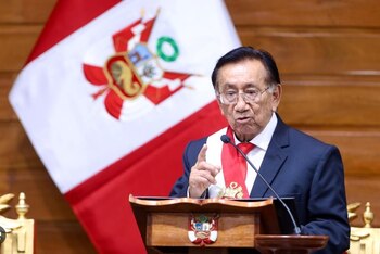 José María Balcázar, un hombre mayor con gafas, traje oscuro y banda presidencial, habla ante un podio con el escudo peruano y una bandera de Perú detrás
