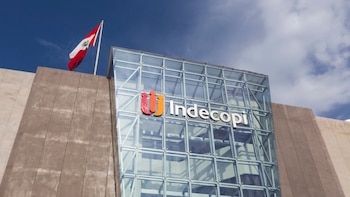 Fachada del edificio del Indecopi con su logotipo sobre vidrio y la bandera de Perú en la cima