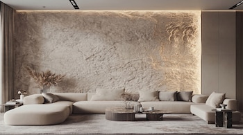 Sofá seccional beige en un salón moderno con pared texturizada iluminada y dos mesas de centro. Un jarrón con ramas secas y cortinas a la izquierda.
