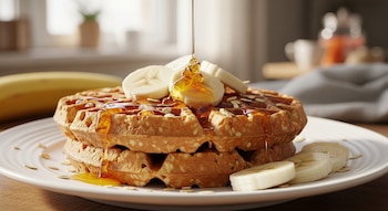 Primer plano de dos waffles de zanahoria y avena apilados en un plato blanco, rociados con miel que gotea y decorados con rodajas de banana y avena.