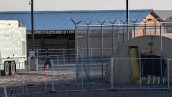 Un hombre camina cerca de un vehículo de la Patrulla Fronteriza. Se ven vallas de seguridad y una tienda de campaña "US" con un tubo de ventilación
