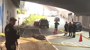 Oficiales de policía resguardan la escena de un hallazgo con cinta de seguridad, conos de tránsito, vehículos y un costal bajo un puente