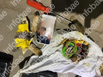 Restos de animal envuelto en tela amarilla y cuerda, una fotografía de persona, una herramienta roja, y una bolsa blanca con semillas, bayas y objetos varios