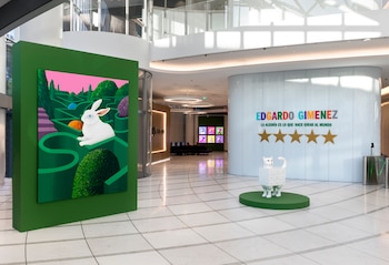 Interior moderno y luminoso con obra de arte. Panel verde con un conejo blanco en un laberinto. Escultura de gato-cómoda junto a un muro blanco con Edgardo Giménez y estrellas