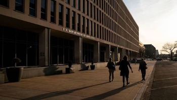 Fachada del edificio del Departamento de Educación de EE. UU. con grandes ventanales oscuros, columnas y personas caminando en la acera al atardecer