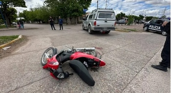 Una motocicleta roja derribada en el asfalto, una camioneta plateada, un automóvil policial y varias personas en una calle