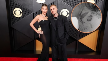Justin y Hailey Bieber posan en la alfombra roja frente a un fondo negro con el logo de CBS. Él viste un traje negro holgado, ella un vestido negro ajustado. Un círculo superpuesto en la parte superior derecha muestra el tatuaje de un melocotón y la palabra "Forever" en el torso de Justin