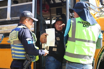 Dos agentes de tránsito e inspectores de la DGT con chalecos reflectantes y un civil con papeles interactúan junto a la puerta abierta de un autobús amarillo