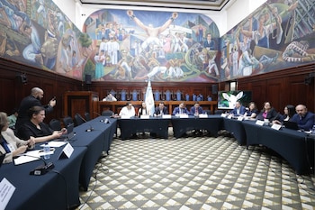 Varias personas sentadas tras una mesa con micrófonos y la bandera de Guatemala frente a un mural y una pantalla con un ternero