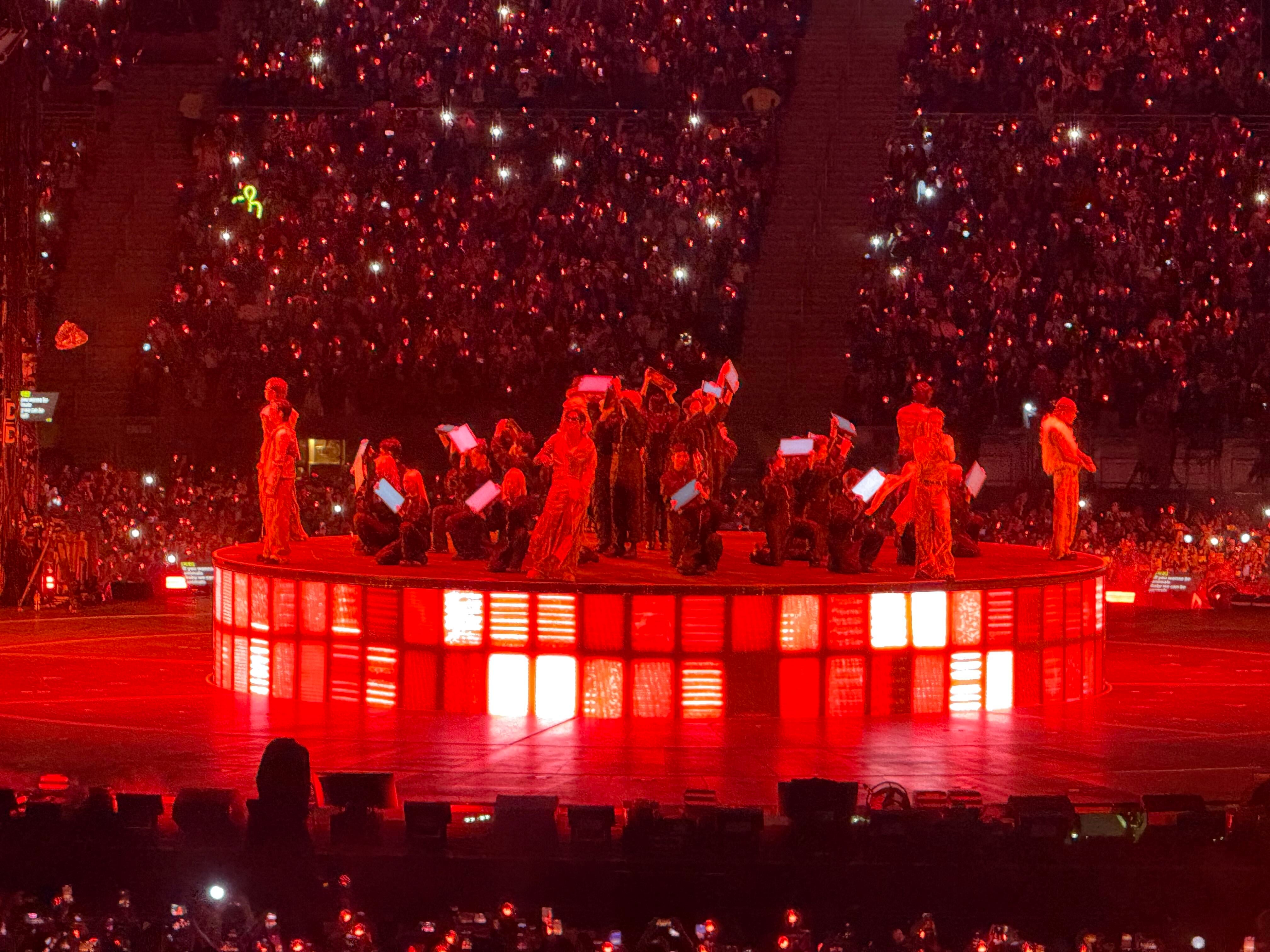 El grupo de k-pop BTS se presenta sobre un escenario iluminado de rojo en el Estadio San Marcos de Lima ante una multitud de fanáticos. (Paula Diaz)