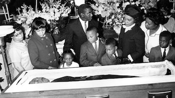 Familiares de Martin Luther King Jr., incluyendo a niños, lo rodean en su ataúd abierto, mostrando su rostro. La imagen es en blanco y negro