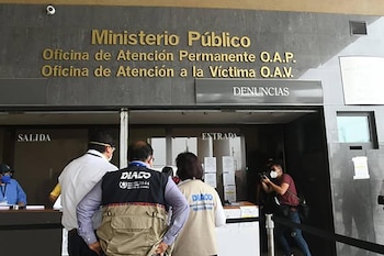 Fachada de un edificio con el letrero 'Ministerio Público, Oficina de Atención a la Víctima'. Varias personas, algunas con chalecos DIACO y mascarillas, entran y salen