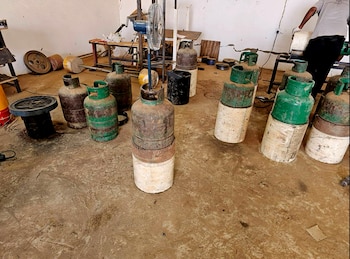 Cilindros de gas verdes y oxidados colocados sobre bases de concreto en el suelo de un espacio de trabajo