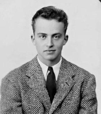 Hombre joven con cabello corto, camisa blanca, corbata oscura y chaqueta de traje estampada posa frente a un fondo liso en una fotografía en blanco y negro