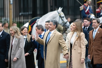 Grupo de personas, incluyendo hombres y mujeres con abrigos de invierno, caminan sonrientes en un evento al aire libre; un caballo blanco con arnés ceremonial se ve detrás