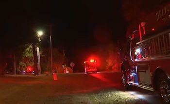 Un camión de bomberos y vehículos de emergencia con luces rojas encendidas en un camino rural durante la noche