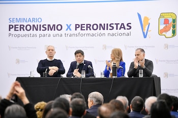 Cuatro personas, tres hombres y una mujer, sentadas en un panel con micrófonos. Detrás, una pancarta con texto y logos. Delante, una audiencia de espaldas