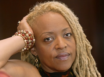 Primer plano de una mujer con rastas rubias, pulseras de cuentas y la mano apoyada en la cabeza
