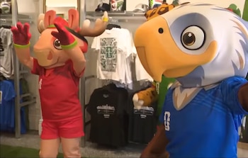 Dos mascotas, una con forma de alce en rojo y otra de águila en azul, posan en el interior de la tienda oficial de la Copa Mundial 2026 con ropa de fondo