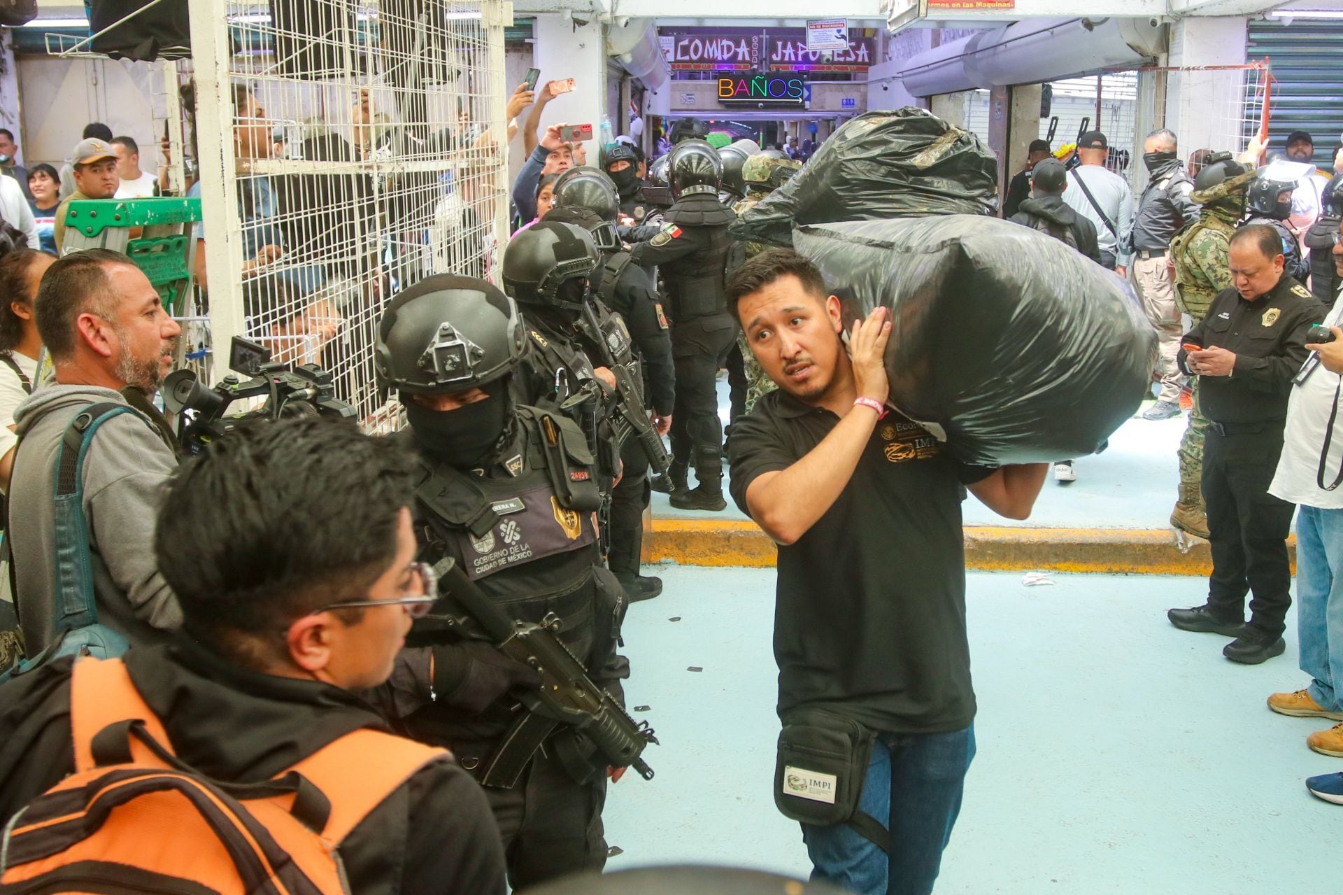 Durante un operativo conjunto en Tepito, Ciudad de México, personal de la Secretaría de Seguridad Ciudadana y el IMPI retiran grandes bolsas de mercancía deportiva presuntamente apócrifa, ante la mirada de civiles. (Cuartoscuro)
