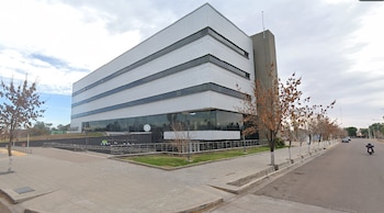 Vista exterior de un edificio alto y moderno del Poder Judicial de Mendoza, con fachada blanca y ventanas oscuras, junto a una acera con árboles y una calle