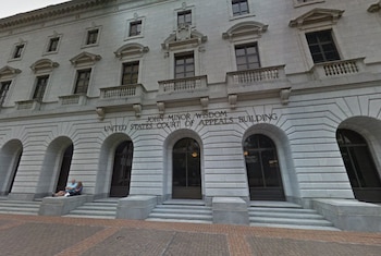 Fachada de piedra del edificio del Tribunal de Apelaciones John Minor Wisdom en Estados Unidos con arcos de entrada y dos personas sentadas