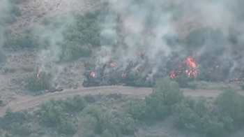 Vista aérea de un incendio forestal con focos de llamas intensas y densas columnas de humo gris en un terreno árido con vegetación