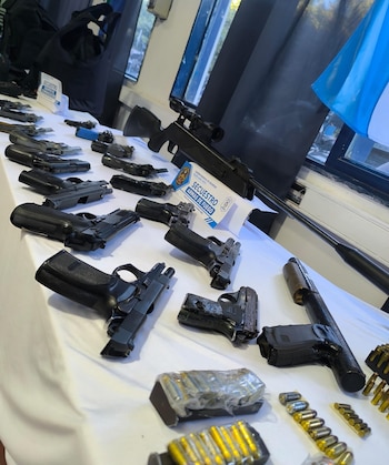 Varias pistolas, cargadores, municiones y un fusil con mira desplegados sobre una mesa con carteles de la Policía de Buenos Aires