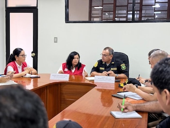 Melina Locatelli Alfaro de INABIF y General Michael Flores Álamo de la PNP sentados en una mesa de reuniones de madera con otros participantes