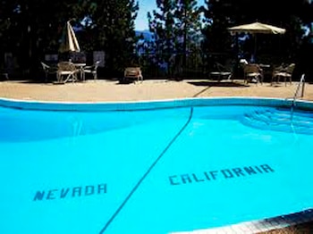 Una piscina azul con una línea negra que la divide. Las palabras "NEVADA" y "CALIFORNIA" están escritas en cada lado. Hay mesas, sombrillas y árboles al fondo