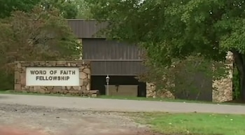 Un letrero de piedra con la inscripción Word of Faith Fellowship ante un edificio marrón rodeado de árboles