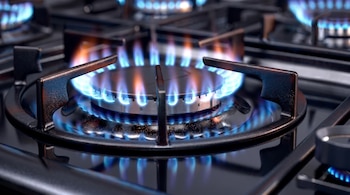 Primer plano de un quemador de estufa de gas encendido con llamas azules vibrantes, rodeado por las rejillas de soporte de hierro fundido.