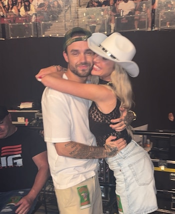 Kate Cassidy lleva un sombrero blanco y abraza a Liam Payne, quien viste una camiseta blanca y una gorra verde