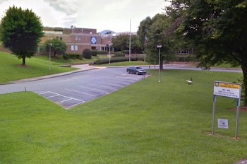 Vista exterior de la Escuela Secundaria McDowell, un edificio de ladrillo con césped verde y árboles, un estacionamiento vacío y un solo auto. Se ve un ganso en el césped