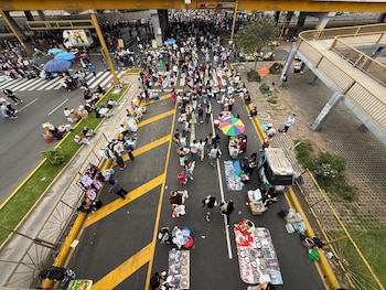 Vista desde una altura de peatones y puestos ambulantes con mercadería desplegada en una calle asfaltada junto a un puente